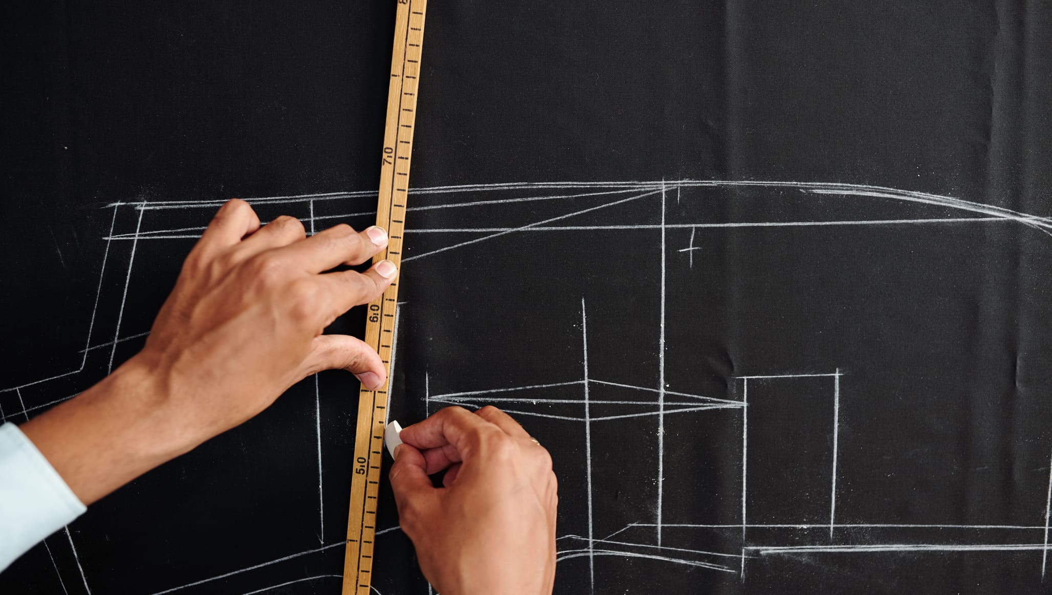Mani che prendono misure con un metro da sarto su una lavagna nera con un disegno tecnico
