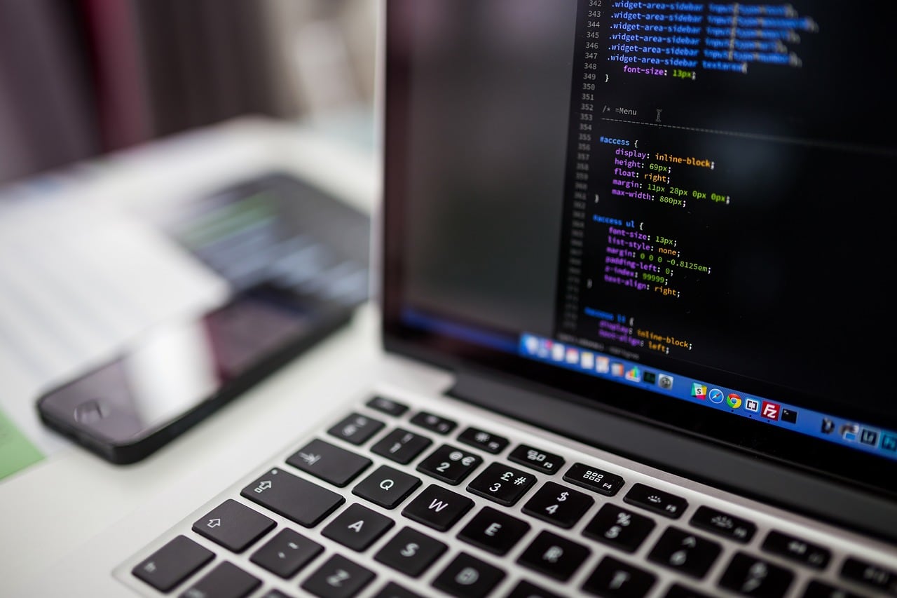 Laptop aperto con codice CSS sullo schermo scuro; accanto, sfocato, uno smartphone appoggiato sulla scrivania.